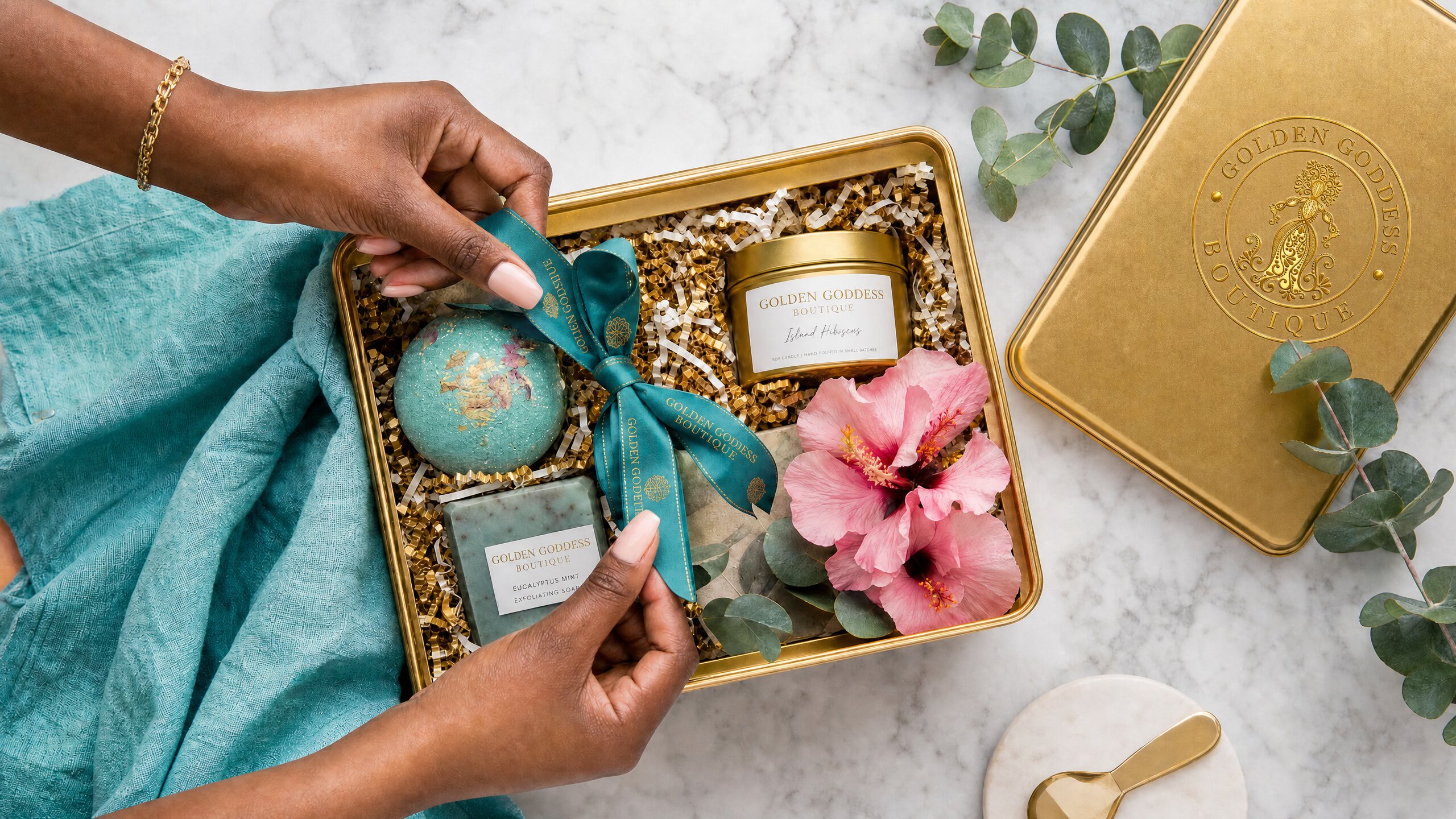 Hands opening a Golden Goddess Boutique gold gift tin with bath bomb, candle, and eucalyptus soap